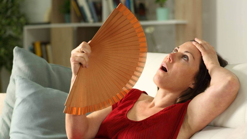 Mulher na menopausa sofrendo onda de calor e se abanando com um leque.